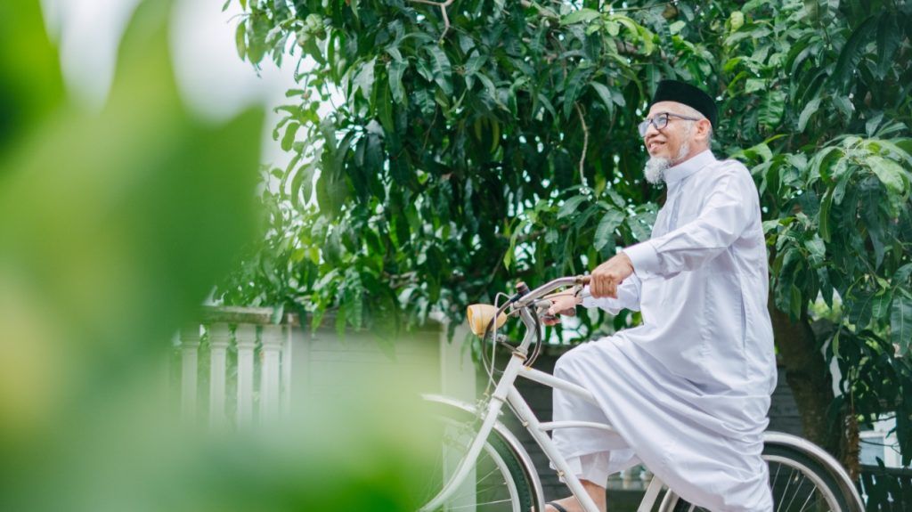 older man riding bicycle through green area