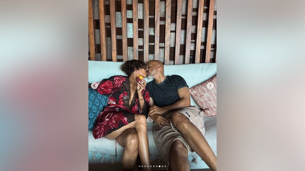 Van Hunt and Halle Berry kissing while sitting on a sofa outside.