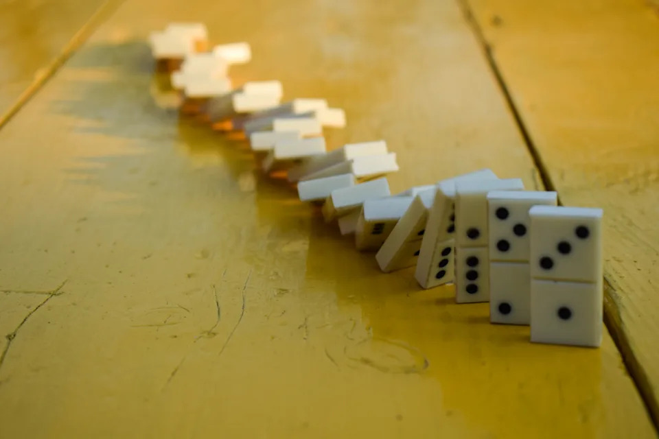 Dominoes falling in a chain reaction, illustrating how the brain chunks habits into a single sequence