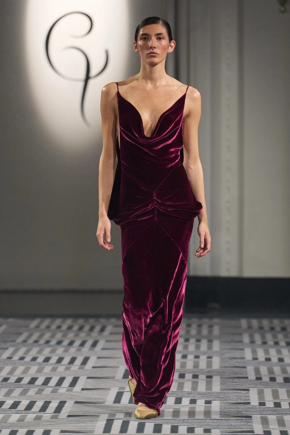 A model walks the runway wearing a deep burgundy velvet gown with a plunging neckline.
