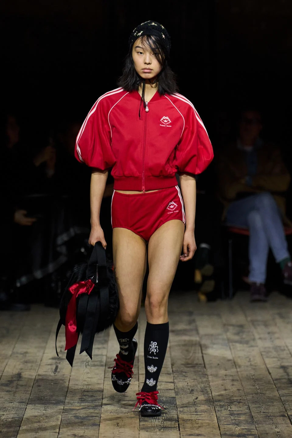 Model walking the runway in a red athletic outfit with puffy sleeves, black accessories, and unique patterned socks.