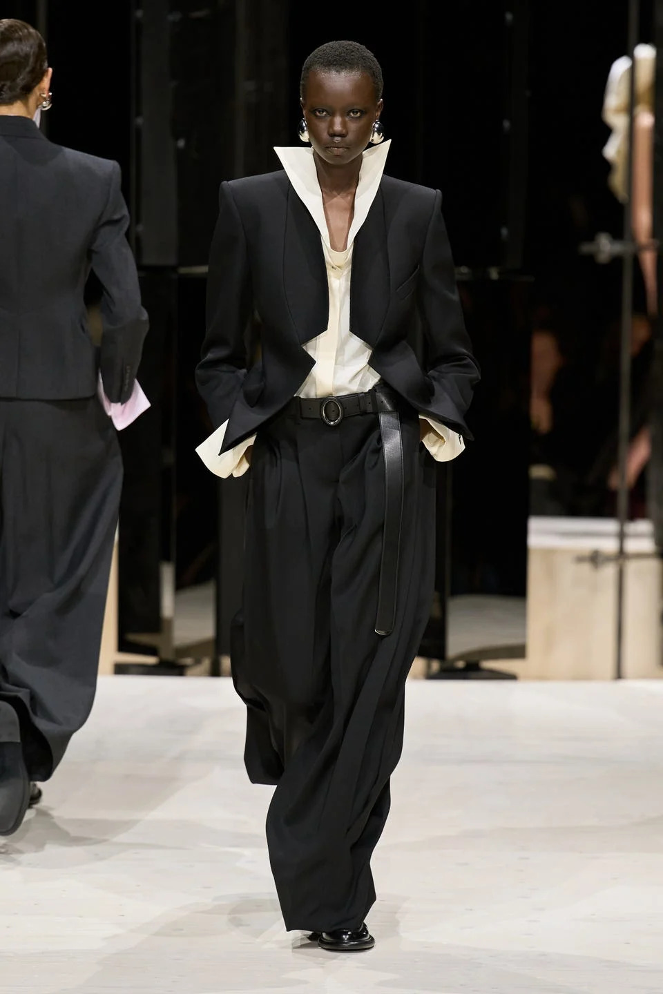Model wearing a black and white suit with a bold collar on the runway.