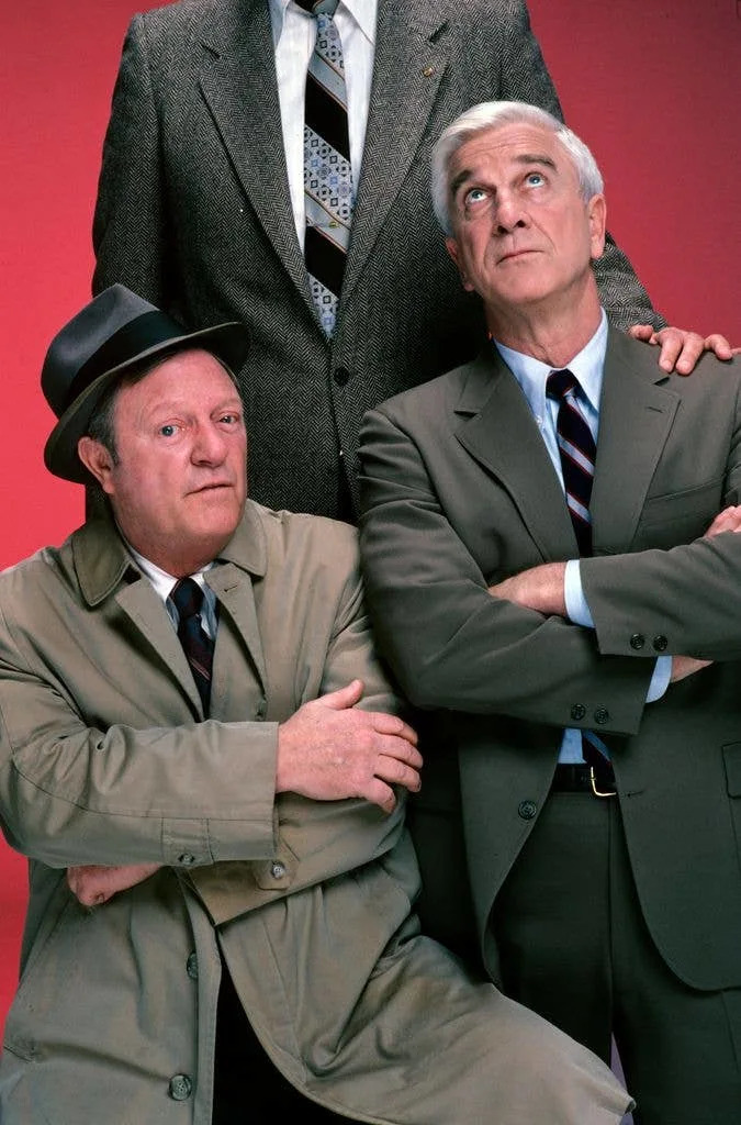 Alan North and Leslie Nielsen pose in front of Tiny Ron for a promotional portrait for 'Police Squad!', dated 1982.