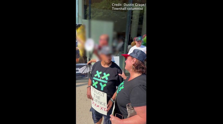 Pro-trans protester waves fan with slur on it toward Sophie Cunningham supporters