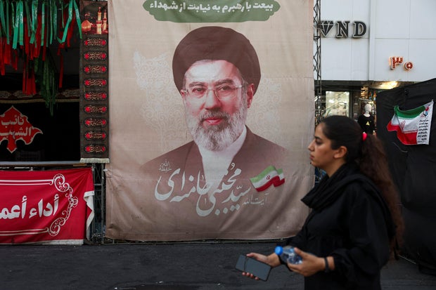A woman walks next to a banner with a picture of Iran's Supreme Leader Mojtaba Khamenei in Tehran
