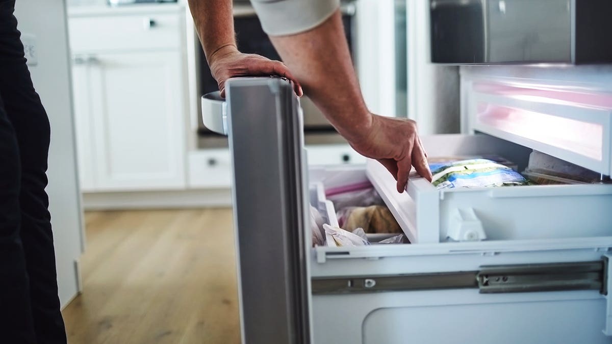 Man looks into an open freezer drawer of a refrigerator.