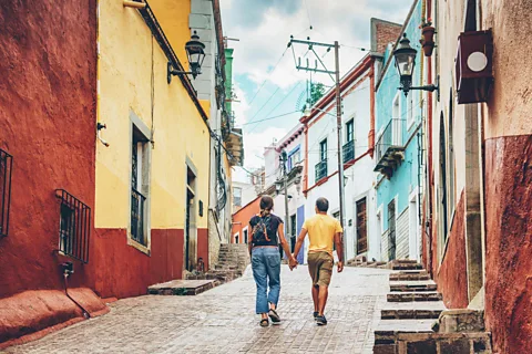 Getty Images Two people walk hand in hand along a cobbled street lined with colourful buildings (Credit: Getty Images)