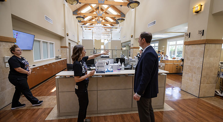 Three people stand and talk inside Rideout Cancer Center, which is a large open space with wooden beam ceilings and a ski lodge feel.