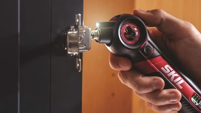 Using a Skil cordless electric screwdriver to screw in a hinge