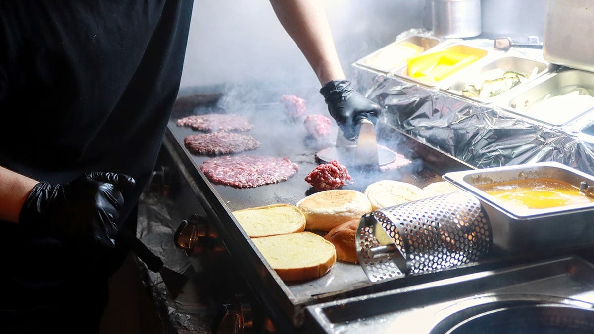 A person smashes a burger on a grill.