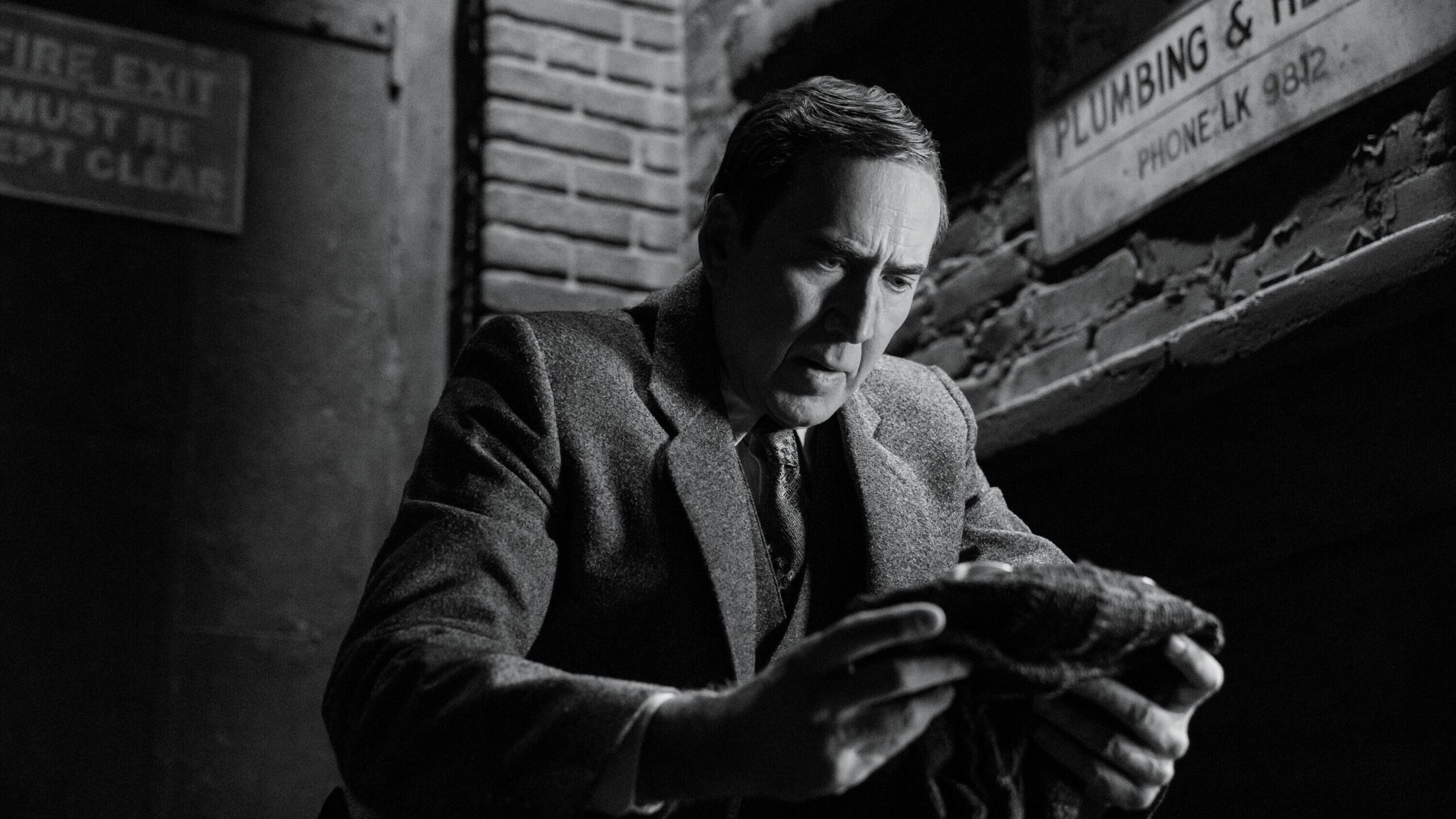 nicolas cage as ben reilly holds a spider-noir mask, looking down.