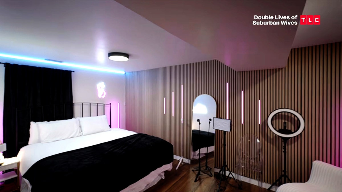 A bedroom features a bed, mirrors, ring lights and pink and blue accent lighting.