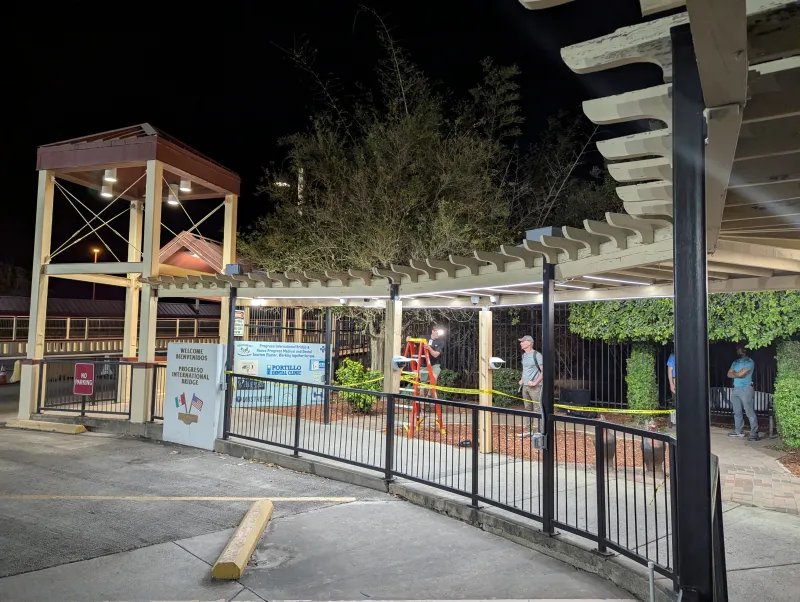 The weathered pergola is well-lit with different lighting fixtures. A man is on a ladder talking to another man. They appear to be working on setting up the cameras and lighting for the live testing.