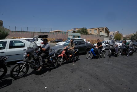 A line of cars and motorbikes queueing on a road.